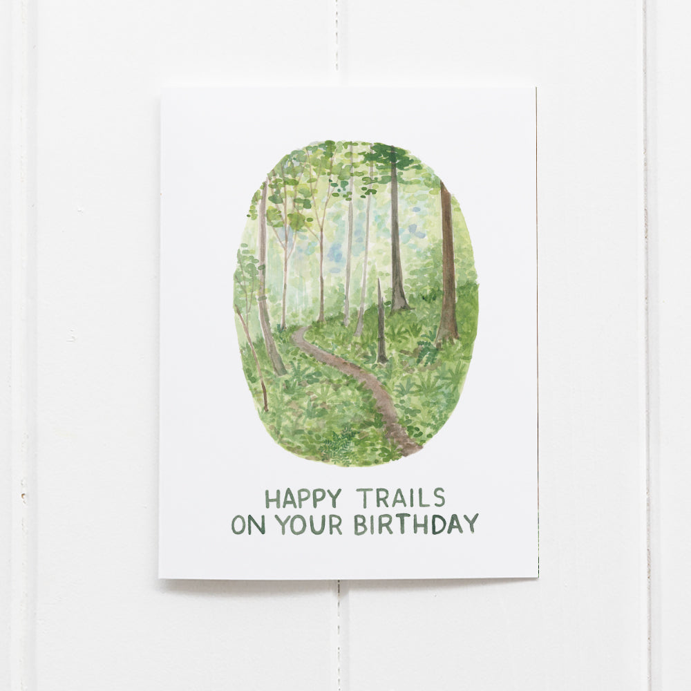 Happy Trails Birthday Card with a watercolor illustration of a Pacific Northwest hiking trail, featuring hand-lettered Happy trails on your birthday message.