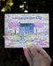 Cozy Birthday Card with watercolor illustration of a cottage and trees, held by a hand, showcasing the card's design and craftsmanship.