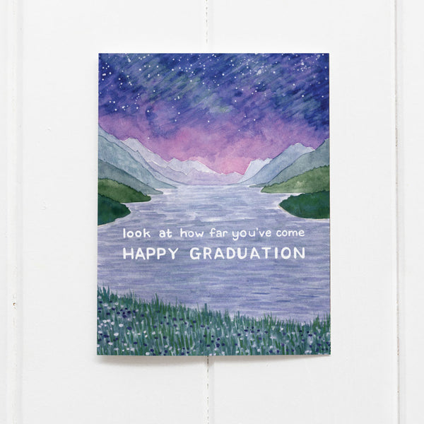 Graduation card with watercolor illustration of lake with many mountains and text reading "look at how far you've come. Happy Graduation"