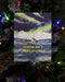 Cozy Holiday Card featuring a watercolor illustration of a cabin in snowy mountains under the Northern Lights, displayed on a decorated Christmas tree.