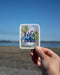 Hafa Adai Sticker: Hand holding a vinyl sticker with a watercolor beach scene and Hafa Adai text, celebrating Guam's Liberation Day.