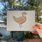 a hand holds a small original watercolor painting of a polish chicken