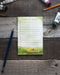 Banana Slug Take It Slow Notepad featuring a checklist design with a pencil on a wooden surface, emphasizing mindful living and relaxation.