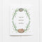 Winter Woodland Holiday Card displaying a watercolor wreath with a sleeping hedgehog and fox, surrounded by greenery, and warm winter wishes in hand-lettered text.