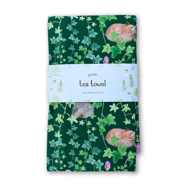 Secret Garden Tea Towel - Organic Cotton Kitchen Towel features a woodland pattern with ivy, foxes, and hedgehogs, packaged with a Yardia paper band.