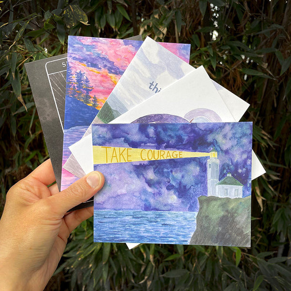 Hand holding the Take Courage Care Pack, a set of five uplifting cards, each featuring inspirational messages, crafted from 100% recycled paper with kraft envelopes.