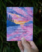 hand holds card reading an anchor when life's untethered with watercolor illustration of sailboat in pacific northwest puget sound at sunset