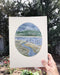 holding an original watercolor painting of a river and water in winter